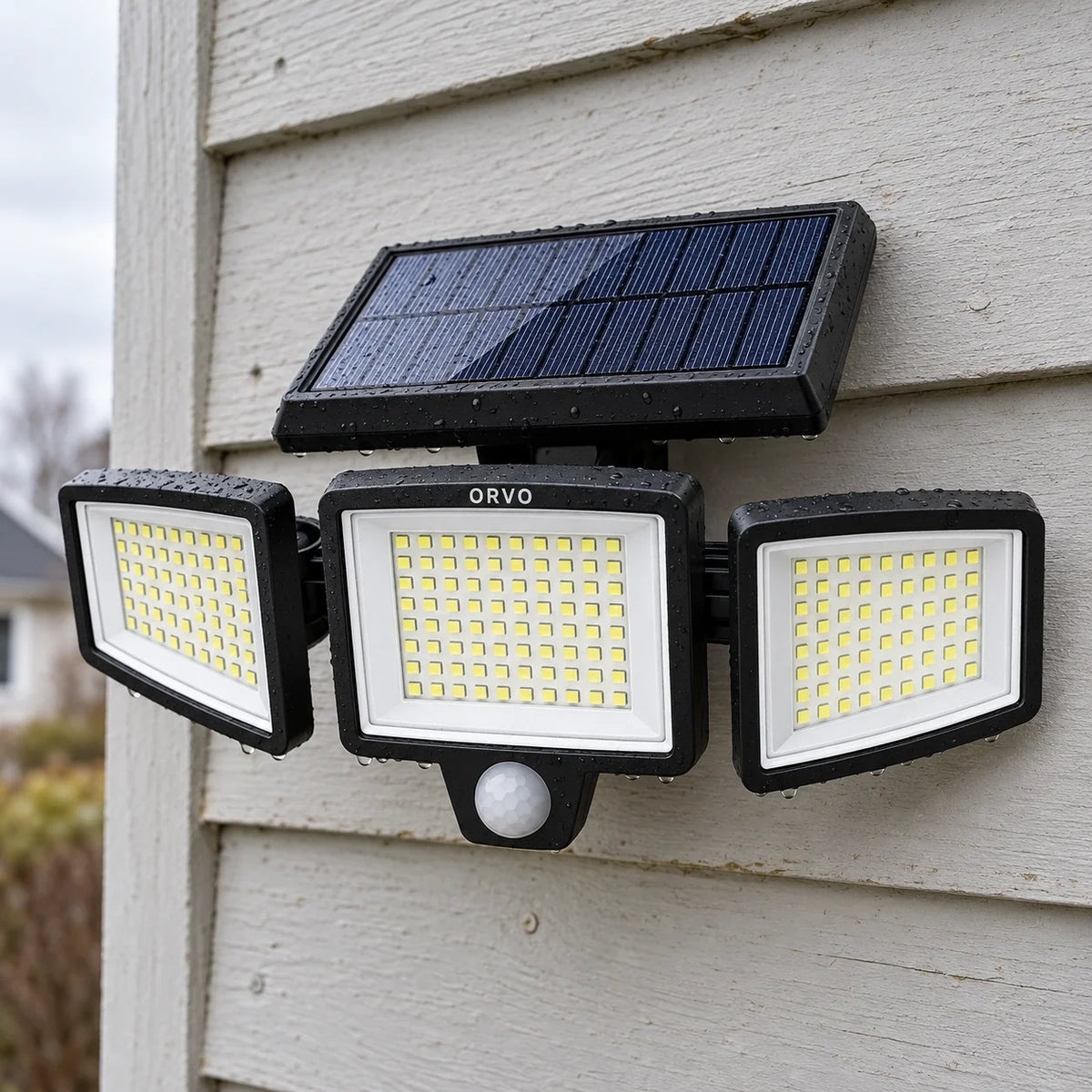 Orvo solcellelampe med tre tændte lampehoveder over en garageport i tusmørket, mens en mand trækker sin cykel ind
